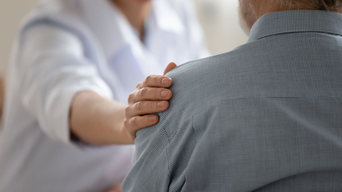 asistenta punand mana pe umarul unui batran pentru sprijin emotional